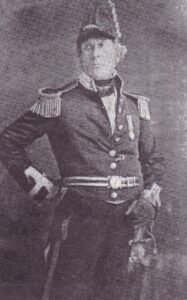 Photograph Naval Captain Thomas Kains circa 1854 in full dress naval uniform with decoration. Caption has Kains as a Cpt (Captain), which may, or may not be unlikely. The Royal Museum at Greenwich displays a very similar uniform which had belonged to purser John Lord who had fallen to his death from high in the rigging. This pattern of uniform had the cuffs and collar changed from white to red (Windsor colours) by HM King William IV in 1832.(image attached for confirmation). While commissioned officers and warrant officers were meant to wear what was essentially the same uniform, rank could be discerned by whether the coat was double- or single-breasted, the arrangement of buttons and the width of gold lace on the collar and cuffs, as well as on the epaulettes. That this is a warrant officer's uniform is indicated by the single-breasted coat with its grouping of eight buttons in pairs. In addition, the purser would have only worn one full epaulette and one scale. In this case the photo of John Kains has two full epaulettes, which may have reflected his promotion to the appointment in 1853 to that of Paymaster on HMS Victory.